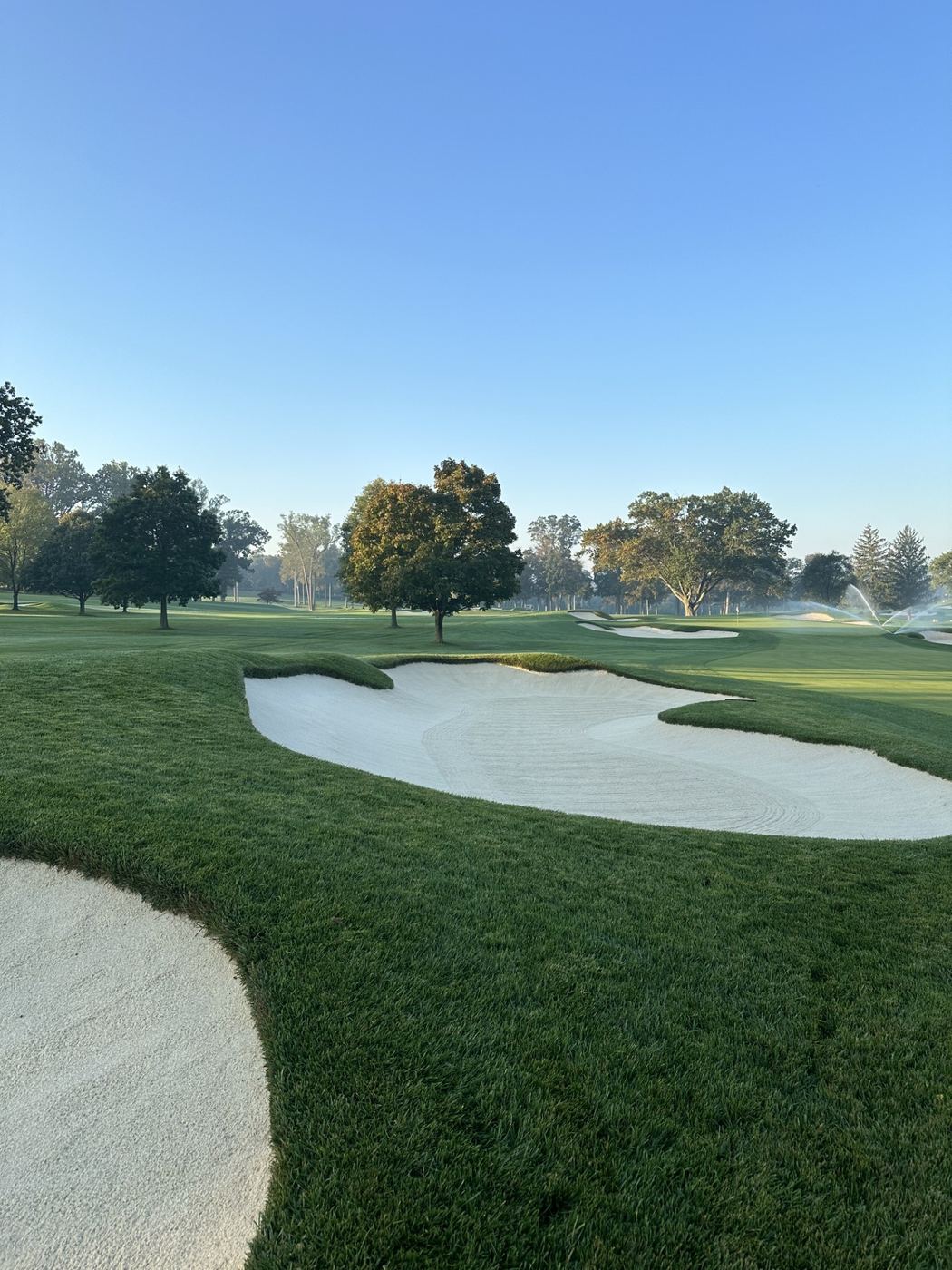 Greenside bunker in early morning light with irrigation heads running in the background