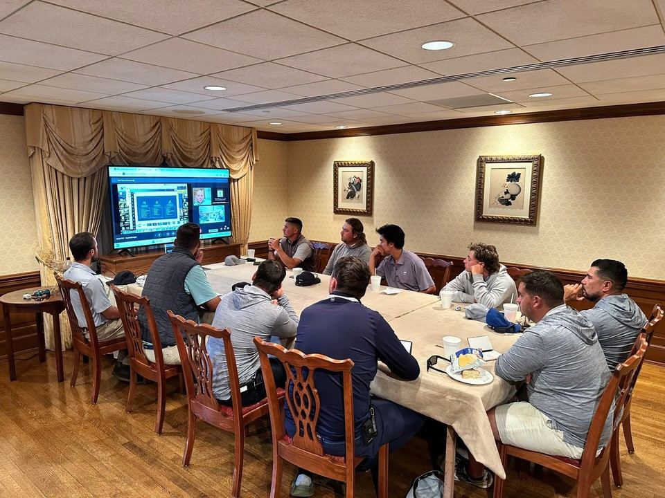 Staff gathered around a conference table watching a virtual training presentation on a large screen