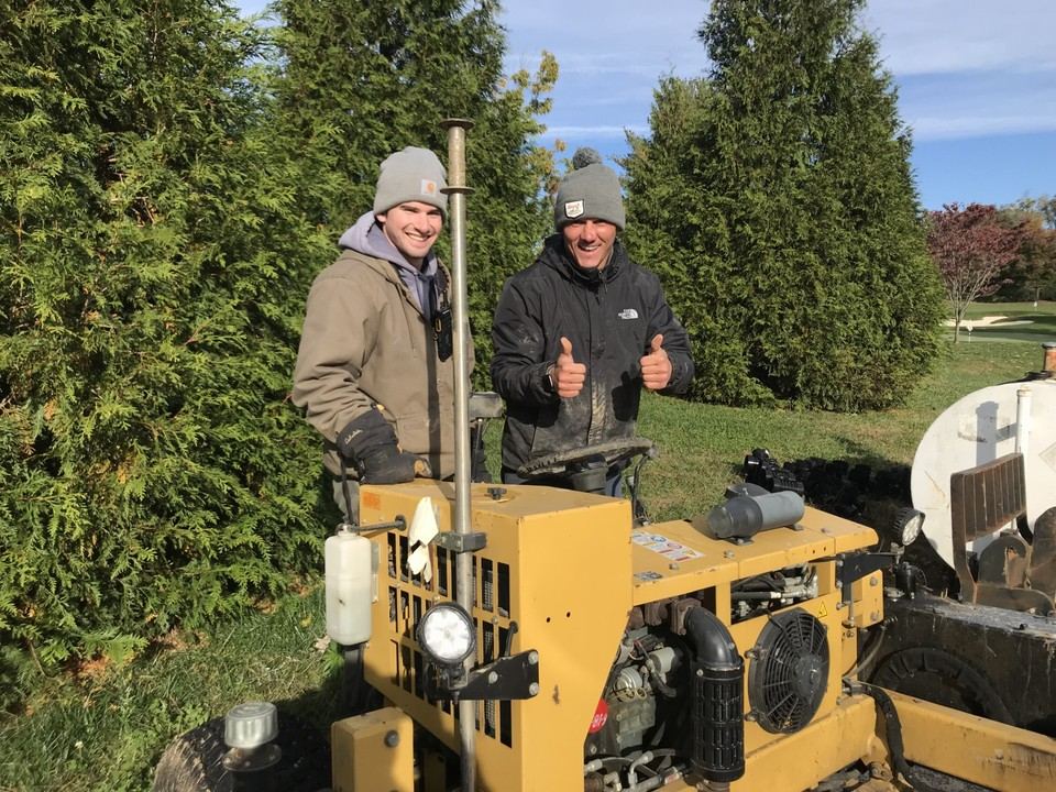 Tom and a colleague giving a thumbs up beside equipment out on the course
