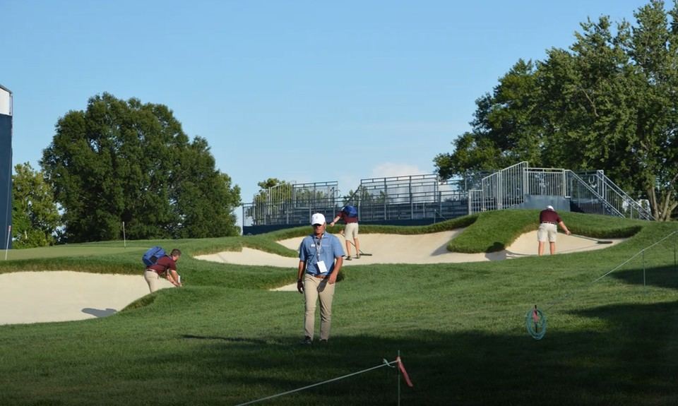 Grounds crew watering a green early in the morning near tournament grandstands