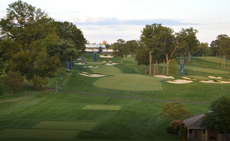 A golf hole prepared for the BMW Championship with tournament infrastructure in the background