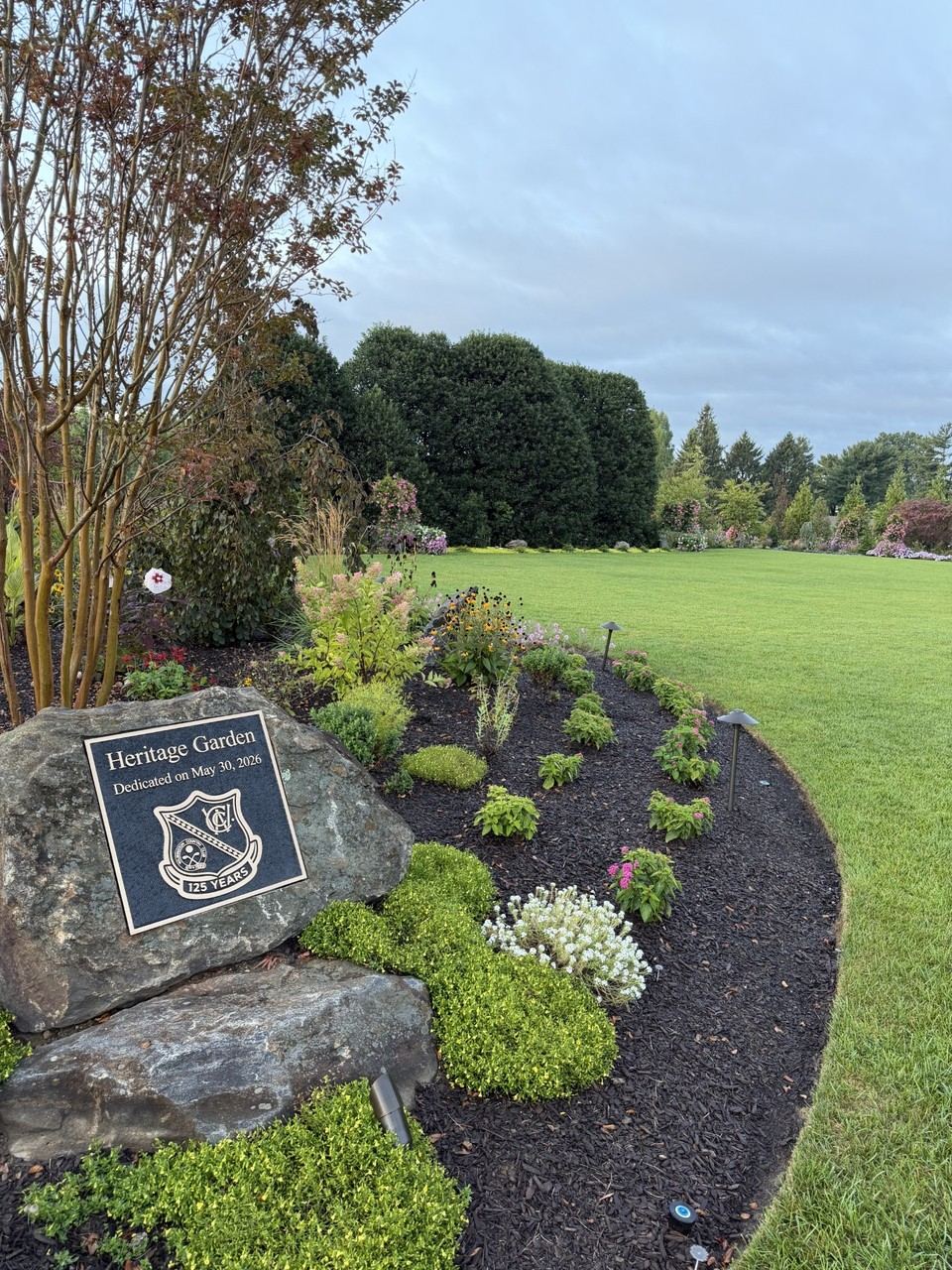 Heritage Garden dedication plaque set into a stone, surrounded by landscaped plantings and open lawn