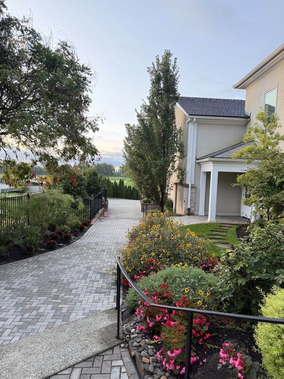 A landscaped paver walkway lined with flowering plants, leading from the bag drop toward the reveal of the South Course's first tee