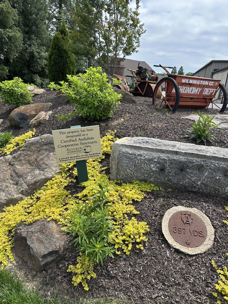 Audubon Cooperative Sanctuary certification sign on the Wilmington Country Club property, alongside a piece of vintage grounds equipment