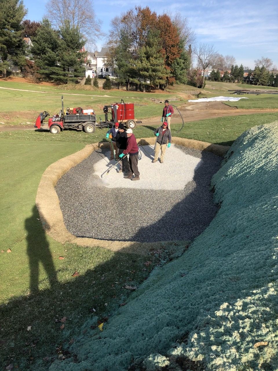 Crew spraying bunker liner and sodded edges before sand is added