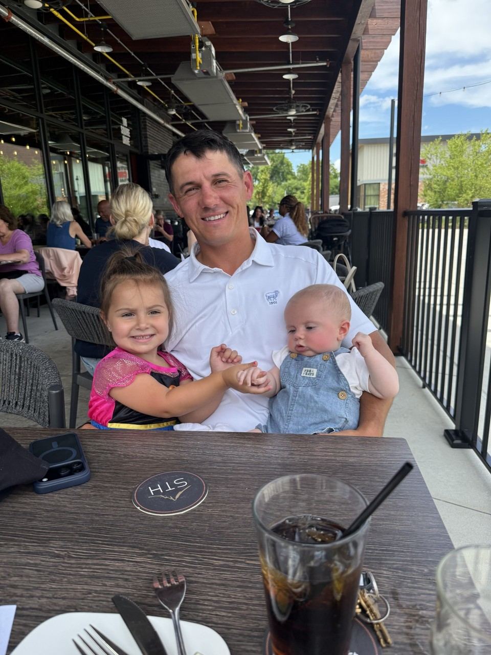 Tom holding his daughter Mackenzie and son Tommy Jr. at an outdoor restaurant table